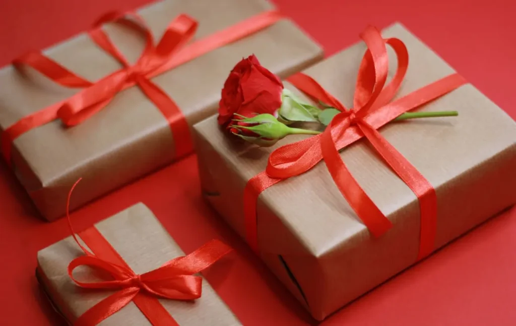Three gift boxes wrapped in solid colored gift papers and tied with red ribbon and red rose in one gift hamper